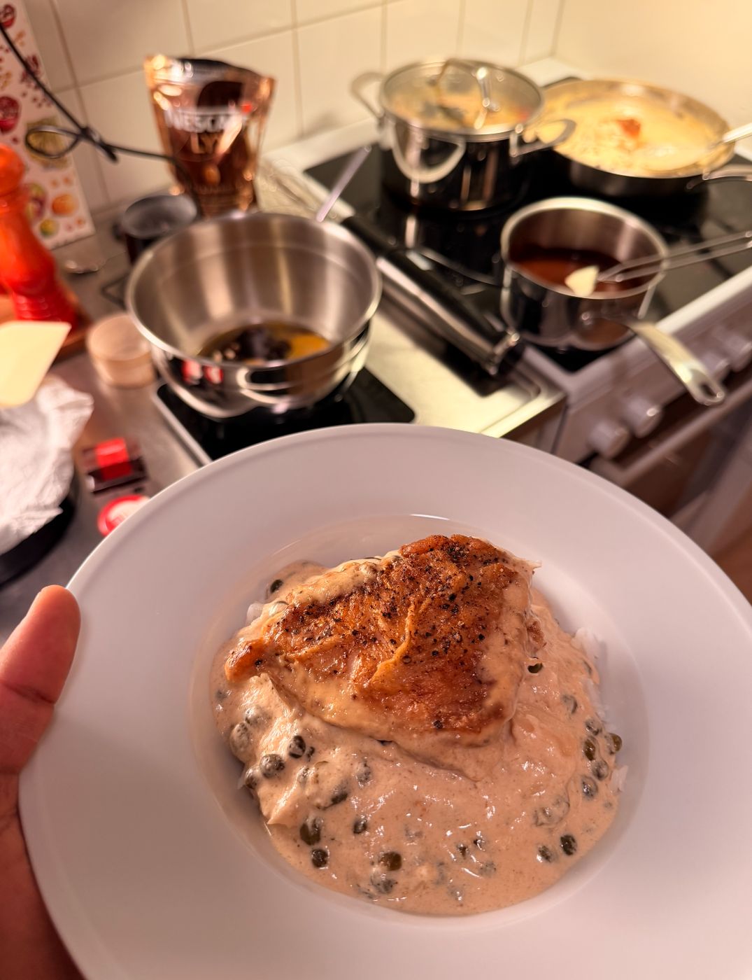 Crisp-skinned chicken on rice with a creamy caper sauce, pots on the stove behind