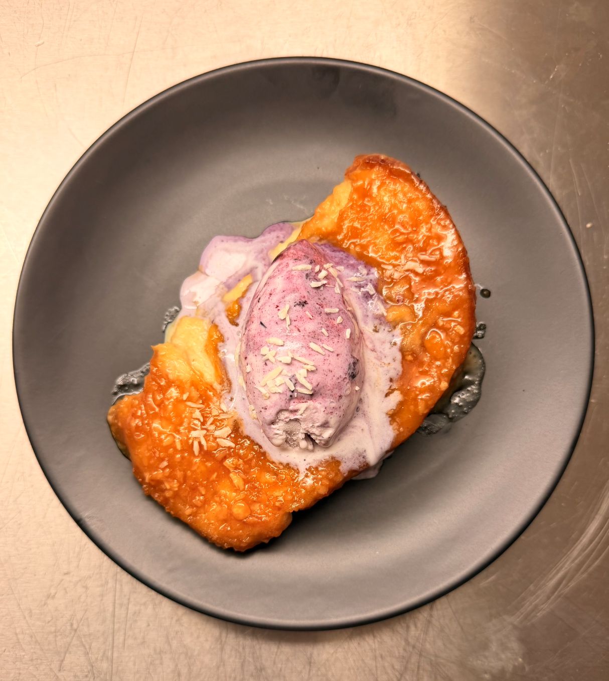 Caramelised pastry with a scoop of blueberry ice cream on a grey plate