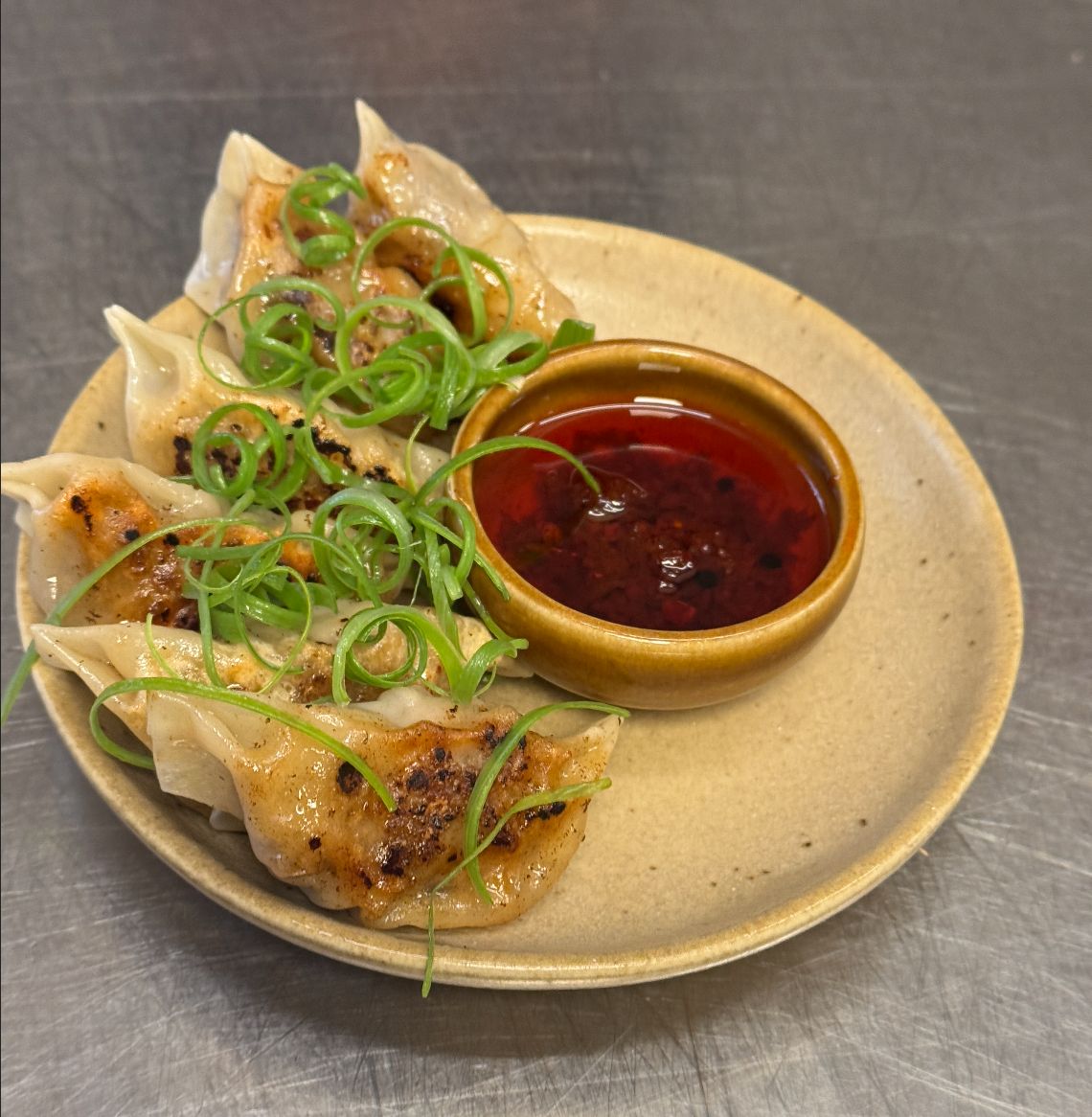 Pan-fried dumplings with spring onion and a small bowl of chili oil