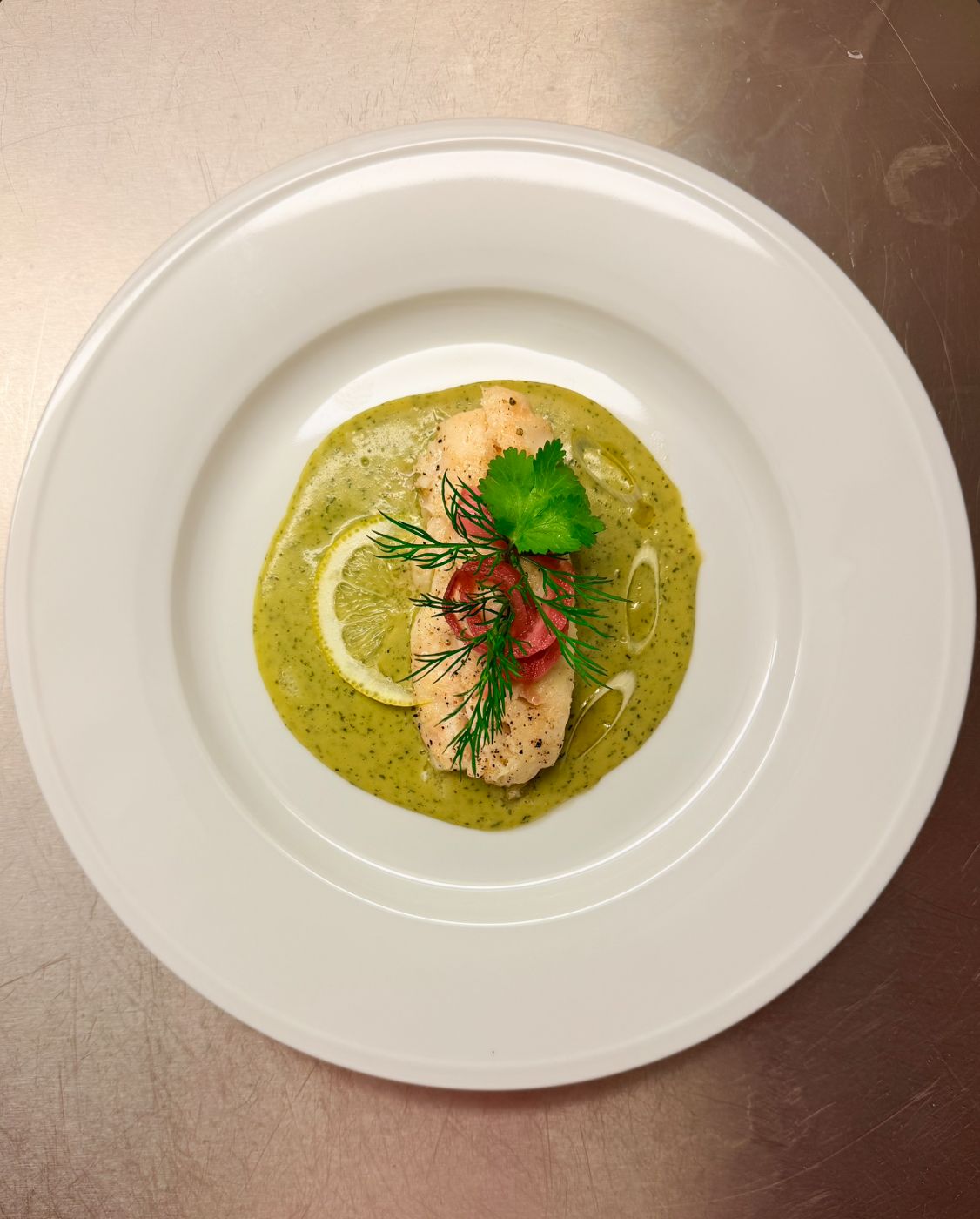 Poached fish in a herb sauce with dill, pickled onion and a lemon slice