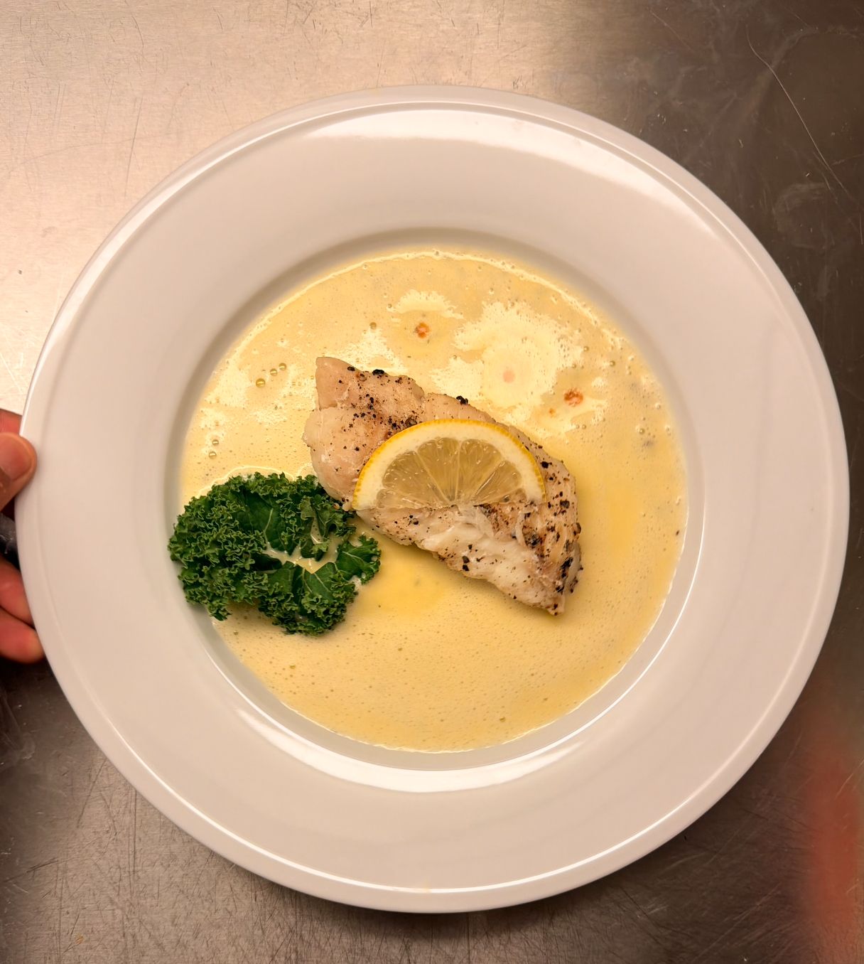 Seared white fish with a lemon slice and kale in a yellow butter sauce