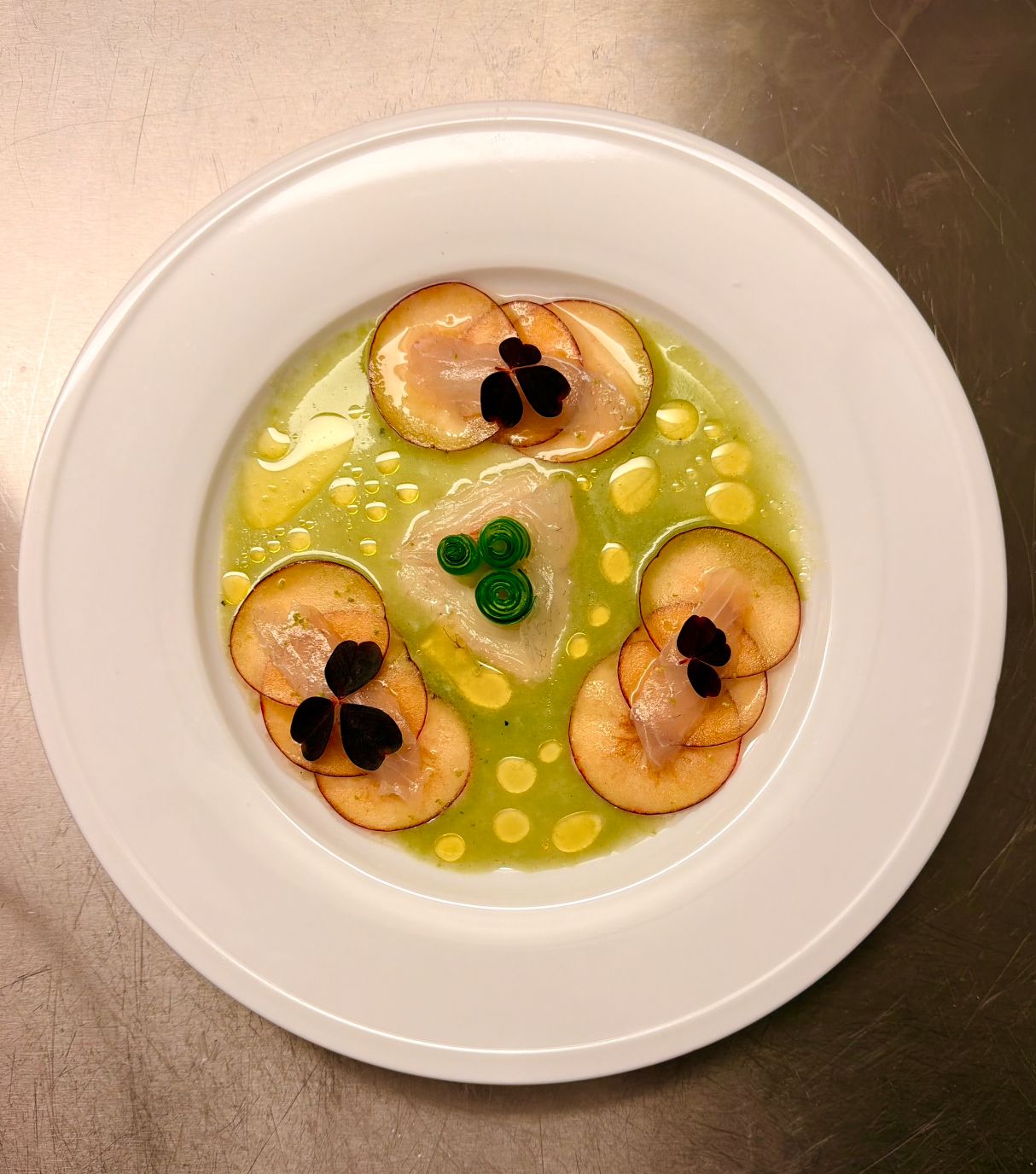 Sliced plum with cured fish, purple oxalis leaves and green sauce on a white plate