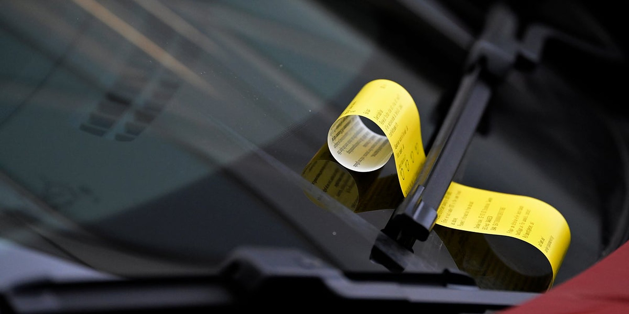 A yellow parking fine curled under a windshield wiper