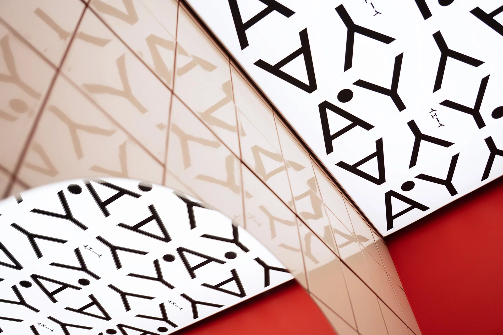 Close-up of the YAY YAY pattern of black Y and A letters on white paper, reflected in pink tiles above a red wall